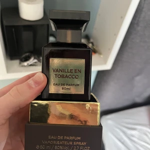 Vanille en Tobacco Eau de Parfum 80ml - Elegant parfymflaska i mörkbrun med guldiga detaljer. Doften kombinerar vanilj och tobak för en unik och sofistikerad upplevelse. Perfekt för den som söker en distinkt och minnesvärd doft.