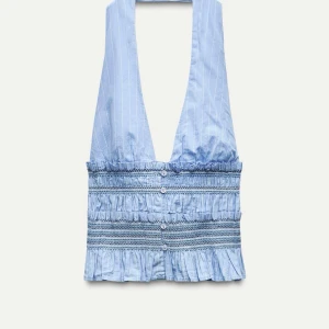 Blå halterneck topp - Snygg blå halterneck topp med smockdetaljer och volangkant. Toppen har ett randigt mönster och djup urringning. Strl S.