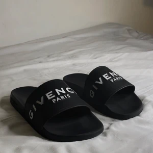 Svarta Givenchy slides  - Snygga svarta slides från Givenchy med vit logotyp på ovandelen. Perfekta inför sommaren eller om du ska utomlands. Tillverkade i syntetmaterial för bekvämligheten och hållbarheten. 