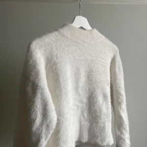 Vit fluffig tröja - Mysig vit tröja med fluffig textur och högre krage. Perfekt för kyliga dagar när du vill hålla dig varm och stilren. Tröjan har långa ärmar och en avslappnad passform. Från HM, använd fåtal gånger!