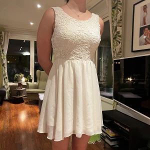 Studentklänning från Model Behavior - Säljer en söt vit klänning från Model Behavior i storlek M. Klänningen har ett vackert spetsmönster upptill och en öppen rygg med knytband. Den är ärmlös och har en luftig kjol som ger en fin silhuett. Perfekt för sommarens festligheter! 🌸