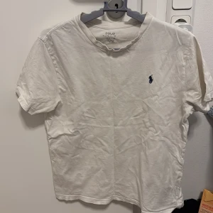 Vit t-shirt från Polo Ralph Lauren - Säljer en klassisk vit t-shirt från Polo Ralph Lauren med den ikoniska broderade loggan på bröstet. T-shirten är kortärmad och tillverkad i mjuk bomull. Perfekt för en avslappnad stil. OBS de finns en jätte liten hål i mitten av t shirten