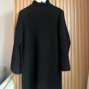 Stickad klänning - Säljer en mysig svart stickad klänning med långa ärmar och hög krage. Perfekt för kyligare dagar och kan stylas med ett bälte för en mer definierad siluett. Enkelt och stilrent plagg som passar till många tillfällen.
