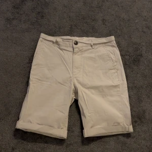 Beige shorts med knappdetaljer - Snygga beige shorts med uppvikta ben och knappdetaljer.  Perfekta för en avslappnad stil. De har en klassisk design med fickor och en bekväm passform.