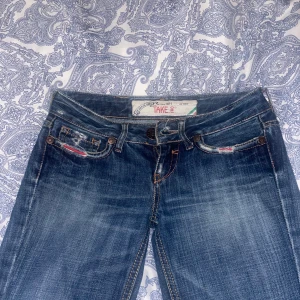 Blå jeans från Take Two - Snygga blå jeans från Take Two med slitna detaljer och kontrastsömmar. De har en klassisk femficksdesign och väldigt låg midja. Perfekta röda detaljer, passar längd 155-165 cm. Storlek 34