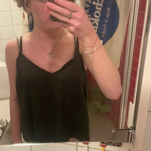 Mörkgrönt linne - Snygg svart linne med smala axelband och v-ringad hals. Perfekt för en stilren och enkel look.