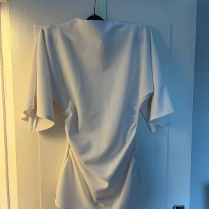 Vit blus från Boohoo - Snygg vit blus från Boohoo med hög hals och utsvängda ärmar. Perfekt för en stilren look. Blusen har en elegant drapering i midjan som ger en smickrande passform. Passar utmärkt till både byxor och kjol. Knappt använd säljes då den är lite för liten!💖 Den har tyvärr sminkfläck på två ställen, kan nog gå bort med fläckborttagning!