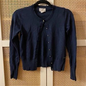 Mörkblå kofta från Holly & White - Säljer en stilren mörkblå kofta från Holly & White. Koftan har långa ärmar och knappar framtill. Perfekt för lager-på-lager under kyligare dagar. Passar både till jeans och kjol.