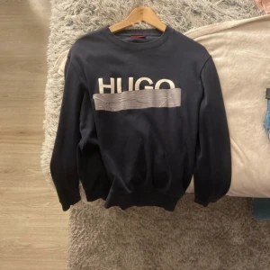 Svart tröja från Hugo Boss - Säljer en stilren svart tröja från Hugo Boss med stort HUGO-tryck på framsidan. Tröjan har långa ärmar och en klassisk rund halsringning. Perfekt för en avslappnad och trendig look. Inga hål väldigt snygg och passar perfekt nu till sommaren och tidigare pris kan diskuteras vid snabb affär bara att höra av er vid frågor eller funderingar eller nya bilder :)😁
