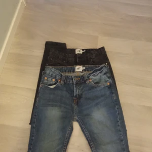 Två par jeans i blått och strl 150 - Säljer två par jeans, ett par i klassiskt blått och ett par i svart. Båda har en straight passform med femficksdesign och knappgylf. Perfekta för en avslappnad stil. Från lager 157 strl 150
