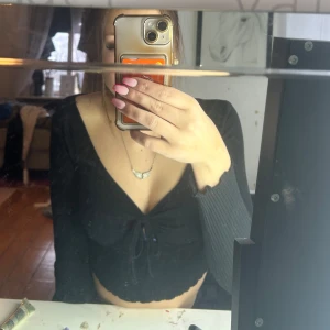 Svart croppad topp från Shein - Säljer en svart croppad topp från Shein med långa ärmar och knytning framtill. Toppen har en ribbad struktur och en v-ringad design. Kommer ej till användning 