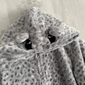 Onepiece Snöleopard  - Mysig heldräkt från Lindex. Storlek 170. Finns en liten fläck på ena ärmmudden som jag inte provat ta bort, och ett litet hack på baksidan. Se bild. Detta är lätt att sy igen! Annars jättefin 