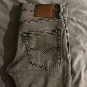 502 från Levi's - Snygga grå jeans från Levi's med klassisk femficksdesign och en liten reva på ena benet. De har en rak passform och är perfekta för en avslappnad stil. Levi's logotyp syns på den bruna läderpatchen baktill.