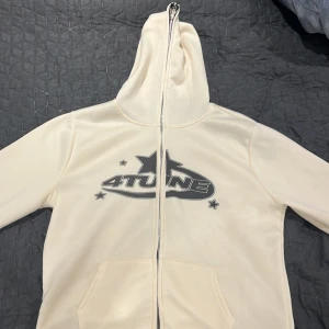 Vit hoodie med tryck från 4tune - Säljer en vit hoodie från 4tune med coolt tryck både fram och bak. Hoodien har en dragkedja och en stor ficka framtill. Perfekt för en avslappnad stil.