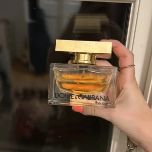 Parfym Dolce & Gabbana The One - Säljer en elegant parfym från Dolce & Gabbana, The One. Flaskan är rektangulär med en gyllene kork och innehåller en gyllene vätska. Perfekt för den som vill ha en lyxig doftupplevelse.