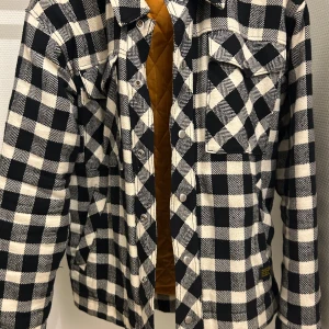 Svartvit rutig jacka från Vaillent - Snygg svartvit rutig jacka från Vaillent med quiltat foder i en kontrasterande färg. Jackan har långa ärmar och knappar framtill. Perfekt för en stilren look.