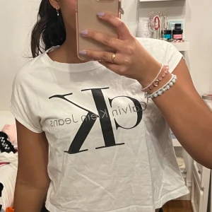 Vit t-shirt från Calvin Klein Jeans - Säljer en stilren vit t-shirt från Calvin Klein Jeans med det ikoniska CK-logotypen tryckt på framsidan. Perfekt för en casual look. T-shirten är kortärmad och tillverkad i mjukt bomullsmaterial.