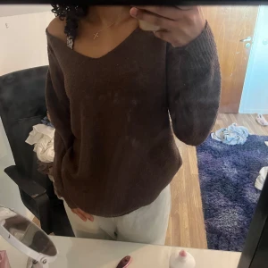 Brun stickad tröja med v-ringning - Mysig brun stickad tröja med v-ringning. Perfekt för kyligare dagar. Tröjan har långa ärmar och en avslappnad passform.