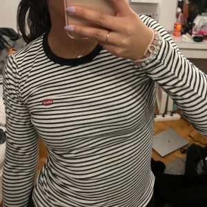 Randig långärmad tröja från Levi's - Säljer en stilren svartvit randig långärmad tröja från Levi's. Tröjan har en rund halsringning med svart kant och det klassiska Levi's-märket på bröstet. Perfekt för en avslappnad look.