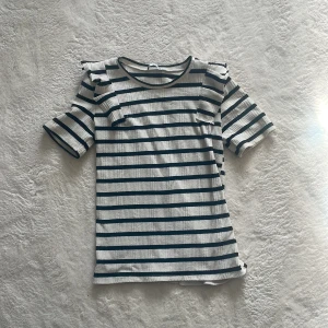 Randig kortärmad topp - Säljer en stilren randig topp med korta ärmar. Toppen har ett klassiskt mönster med mörkblå ränder på en vit bakgrund. Perfekt för en avslappnad stil. Strl m men skulle säga att det är mer s