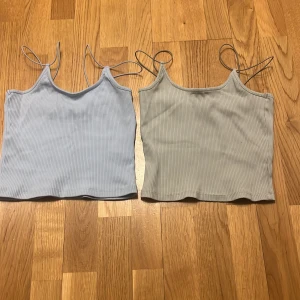 Två ribbade linnen i blått och grönt - Säljer två snygga ribbade linnen i ljusblått och ljus grön. Båda har smala axelband och en croppad passform, perfekta för sommardagar. De är tillverkade i ett mjukt och stretchigt material som ger en bekväm känsla.