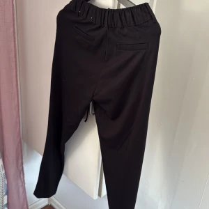 Svarta byxor från Esmara - Snygga svarta byxor från Esmara med elastisk midja och snörning. Byxorna har en stilren design med fickor baktill och är perfekta för en avslappnad look. Passar bra till både vardag och mer uppklädda tillfällen.