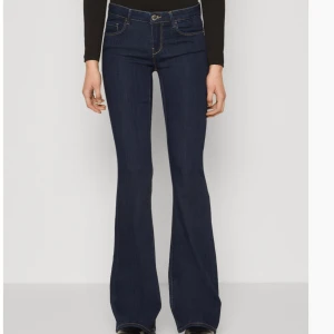 Lågmidjada utsvängda jeans från ONLY - Slutsålda snygga mörkblå utsvängda jeans från ONLY med låg midja. STORLEK xxxs/ längd 32. Perfekta för en retro look med en modern twist. Tillverkade i denim med klassisk femficksdesign och knappgylf. De finns tecken på användning, det finns inga hål.