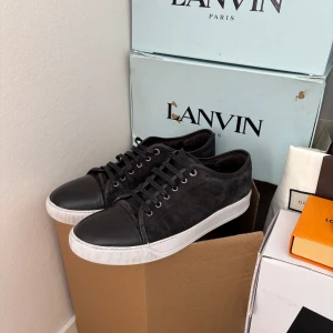 Svarta sneakers från Lanvin storlek 45 - Snygga svarta sneakers från Lanvin med en stilren design. Skorna har en kombination av skinn och syntetmaterial med en vit sula och snörning framtill. Perfekta för en trendig look. Priset går att diskutera vid snabb äffär. og dustbag medföljer vid köp. Skicket är okej men finns några defekter 