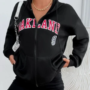 Svart hoodie med dragkedja och tryck - Snygg svart hoodie med dragkedja och texten 'OAKLAND' i rött och vitt på framsidan. Tröjan har en luva och långa ärmar, perfekt för en avslappnad stil. Nummer 9 tryckt i vitt ger en sportig touch.