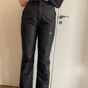 Svarta täckbyxor från Lager 157 - Säljer ett par svarta täckbyxor från Lager 157. De är högmidjade med dragkedja och knapp framtill. Byxorna har en rak passform och är perfekta för kalla dagar. Praktiska fickor med dragkedja på sidorna.