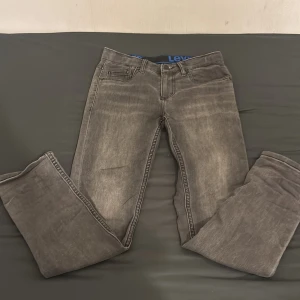 Grå jeans från Levi's - Snygga grå jeans från Levi's med klassisk femficksdesign och knappgylf. De har en rak passform och är perfekta för en avslappnad stil. Levi's-loggan syns tydligt på bakfickan.