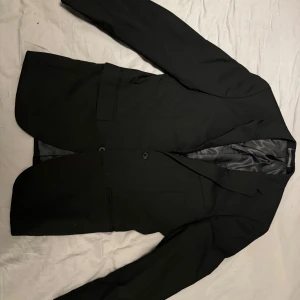 Svart kavaj från Riley - Klassisk svart kavaj med en tidlös design. Den har en figursydd passform och är perfekt för både formella och avslappnade tillfällen. Kavajen har en traditionell krage, knäppning fram och praktiska fickor. Skick: bra skick Storlek: 44 Ord. Pris: 999 SEK  Din stil: spara inlägget så du inte missar denna kappa Inte din stil: Kolla min profil. Du kommer hitta något för alla kön och åldrar.