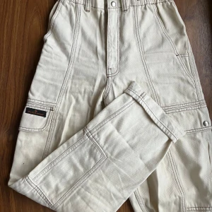  Cargopants från BDG - Snygga beige cargopants från BDG med elastisk midja och flera praktiska fickor. Byxorna har en avslappnad passform och är perfekta för en casual look. Tillverkade i ett slitstarkt material med kontrastsömmar som ger en cool detalj.