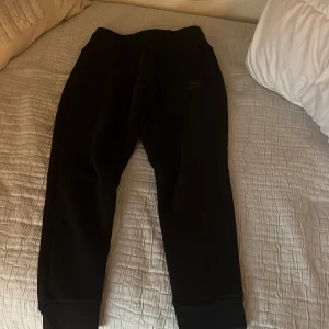 Svarta mjukisbyxor från Nike - Säljer ett par svarta mjukisbyxor från Nike. Byxorna har en bekväm passform med snörning i midjan och är perfekta för en avslappnad stil. De är tillverkade i ett mjukt material som ger en skön känsla.