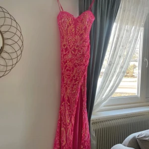 Rosa glittrig långklänning - Säljer en fantastisk rosa långklänning med glittriga detaljer och smala axelband. Klänningen har en elegant passform och ett vackert mönster som verkligen fångar ögat. Perfekt för speciella tillfällen!