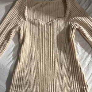 Beige ribbad tröja - Säljer en stilren beige ribbad tröja med långärmad design. Tröjan har en fyrkantig halsringning och är perfekt för en elegant look. Passar bra till både jeans och kjol.