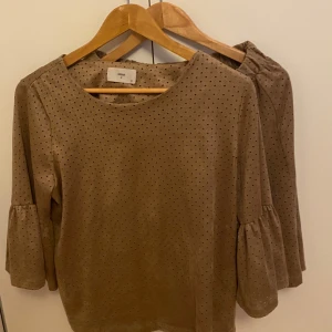 Beige set med kjol och topp från Minimum i mockaimitation - Säljer en söt beige topp med kjol från Minimum. Blusen har trekvartsärmar med volangdetaljer och en rund halsringning. Perfekt för en stilren look.