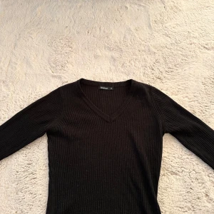 Svart ribbad tröja från Boohoo - Säljer en stilren svart ribbad tröja från Boohoo. Tröjan har en v-ringad hals och långa ärmar, perfekt för en enkel och snygg look. Passar bra till både jeans och kjol. Hör av dig vid intresse!