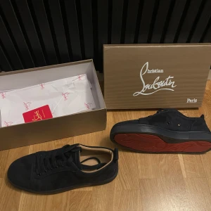 Christian Louboutin sneakers - Snygga marinblå sneakers från Christian Louboutin med den ikoniska röda sulan. Skorna har en stilren design med snörning och är tillverkade i mocka. Perfekta för dig som vill ha en touch av lyx i vardagen. Skick 9/10 då sulan är smått smutsig(går lätt att få bort). 
