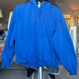 Blå hoodie - Säljer en klassisk blå hoodie med känguruficka och justerbar huva från Weekday.