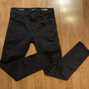 Svarta jeansbyxor från Replay - Snygga svarta jeansbyxor från Replay i modellen Anbass. De har en klassisk femficksdesign med knapp och dragkedja framtill. Perfekta för en stilren look. Lite slitna på vissa ställen. Storlek 29/30