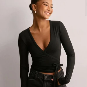 Svart omlottopp från Nelly - Snygg svart omlottopp från Nelly med långa ärmar och knytning i midjan💕