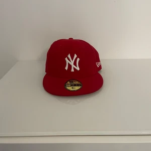 Röd keps från New Era - Snygg röd keps från New Era med broderad vit logga framtill. Perfekt för att ge din outfit en sportig touch. Kepsen har en klassisk passform och är tillverkad i bomull för en bekväm känsla.