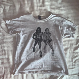 Vit t-shirt med tryck från in print we trust - Säljer en vit t-shirt från in print we trust med ett svartvitt tryck av kate moss och naomi campbell på framsidan. T-shirten är kortärmad och tillverkad i bomull. Perfekt för en avslappnad stil.