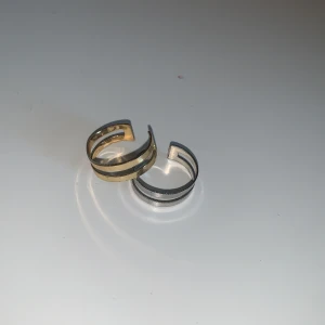 Tvåfärgade öppna ringar - Säljer två stilrena öppna ringar i guld och silver. Ringarna har en modern design med dubbla band och är justerbara för att passa olika storlekar. Perfekta för att ge en elegant touch till din stil.