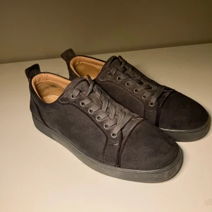 Svarta sneakers från Christian Louboutin - Snygga svarta sneakers i mocka från Christian Louboutin med den ikoniska röda sulan. Skorna har snörning och en stilren design som passar perfekt för en trendig look. Hör av er vid frågor!
