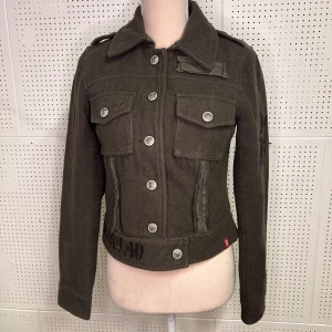 Mörkgrön jacka med knappar - Snygg mörkgrön jacka med knappar och två bröstfickor. Jackan har en klassisk krage och axelklaffar. Perfekt för en stilren look.