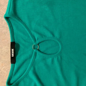 Grön ribbad topp från Bik Bok  - Snygg grön ribbad topp från Bik Bok med långärmad design. Toppen har en unik detalj med en ring vid halsen som ger en extra touch. Perfekt för att lägga till lite färg i garderoben!😁