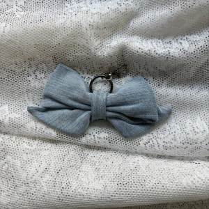 Ljusblå rosett i denimtyg  - Charmig grå rosett i tyg. Perfekt som en söt accessoar för att dekorera väskor eller nycklar. Med grått metallfäste. (Vi erbjuder att möta upp i Stockholms innerstad, Huddinge, Tyresö och Lidingö) 