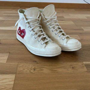 Cdg Converse  - Snygga vita höga sneakers från converse x cdg. Skorna har klassisk snörning och en rund tå. Perfekta för en stilren och trendig look.